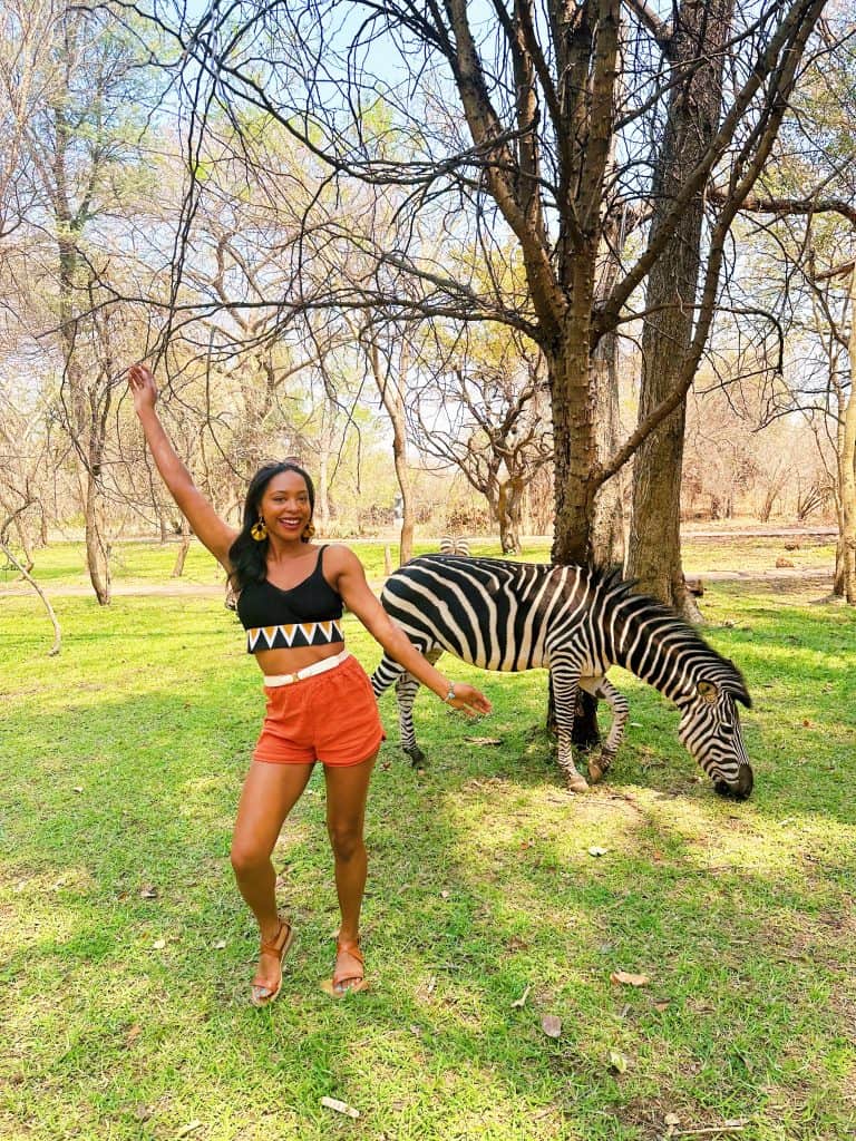 Woman standing next to zebra on Avani Victoria Falls resort property