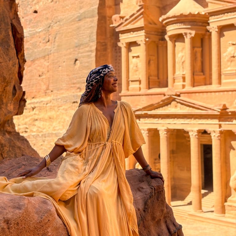 A woman in a yellow dress sitting on a rock in front of the ancient city of Petra
