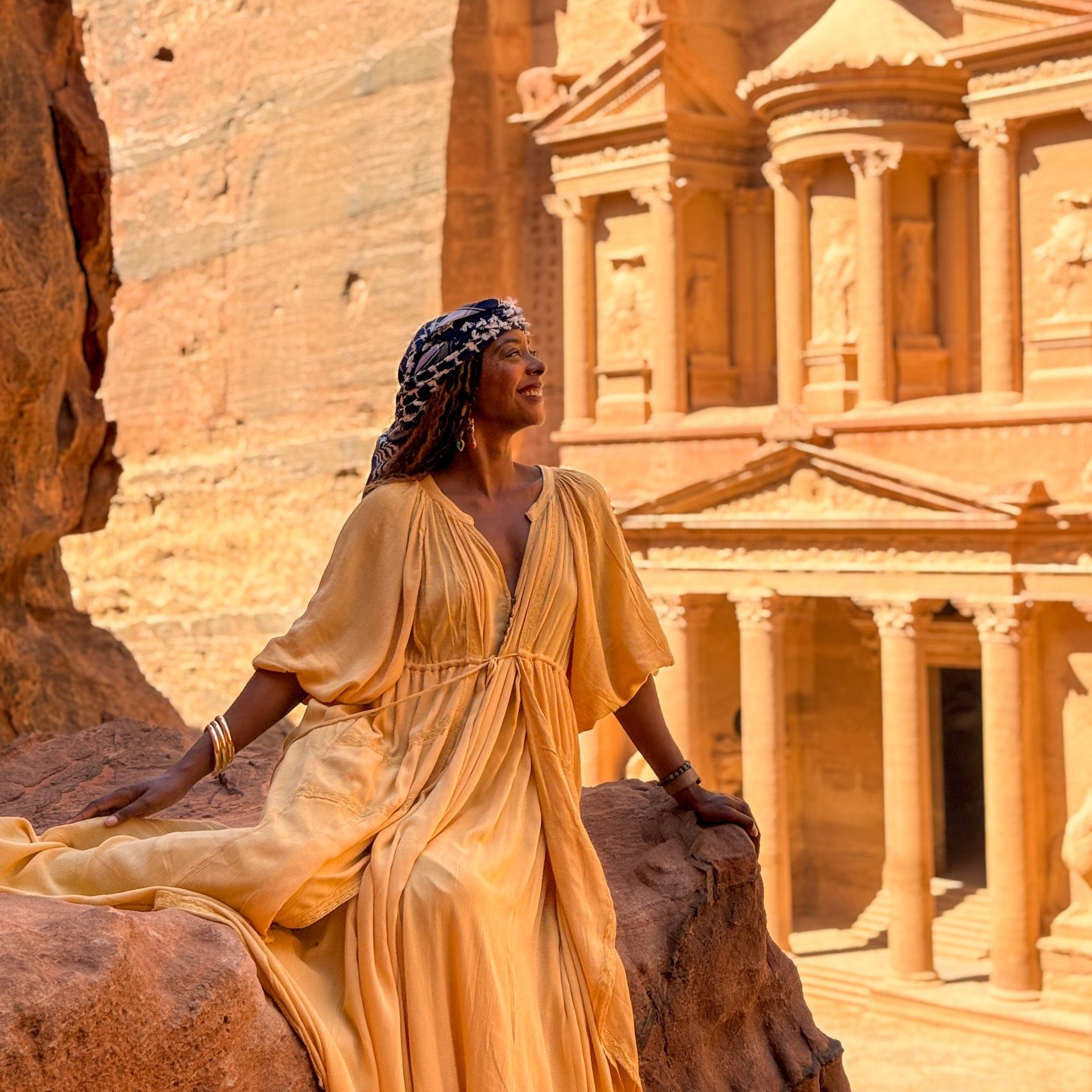 A woman in a yellow dress sitting on a rock in front of the ancient city of Petra