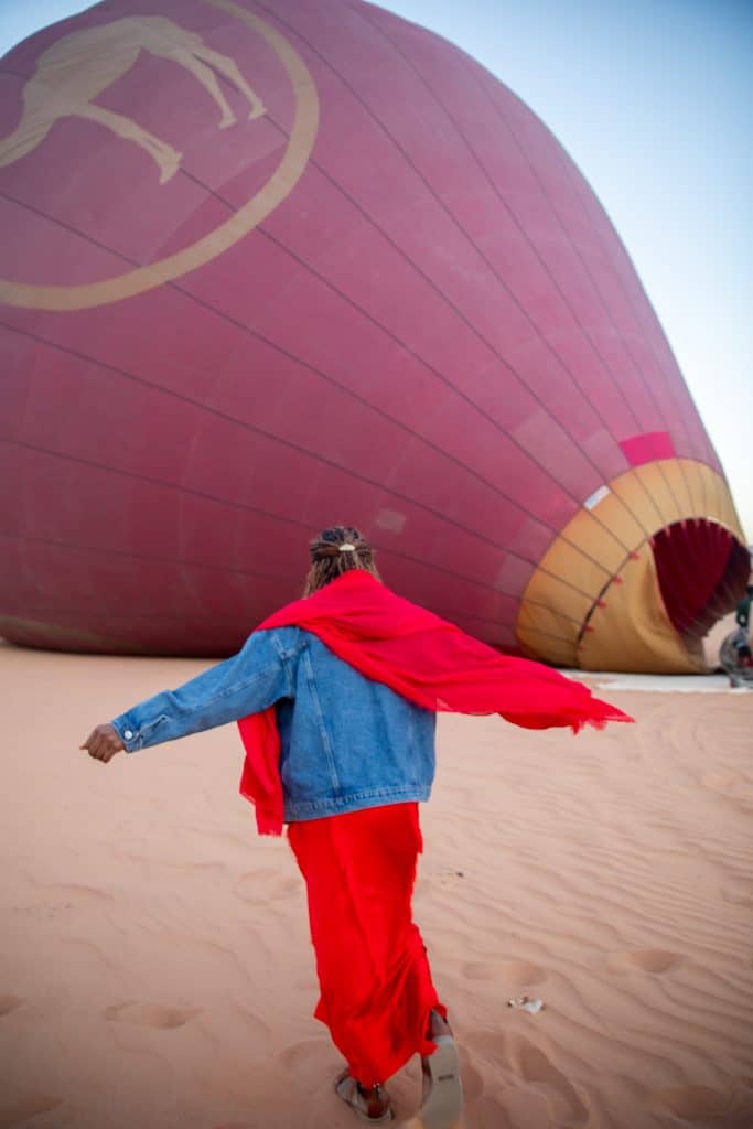 A woman in a red cape running towards a hot air balloon.