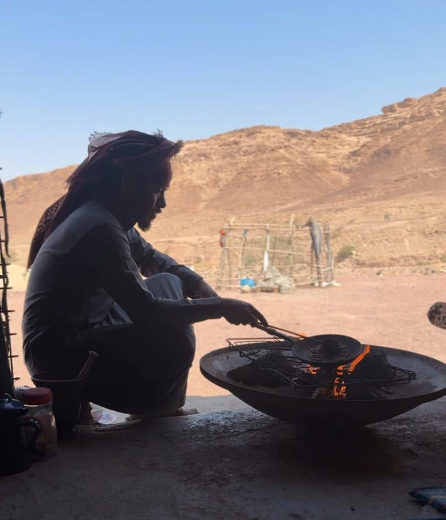 A man making Arabic coffee on a fire pit in the desert.