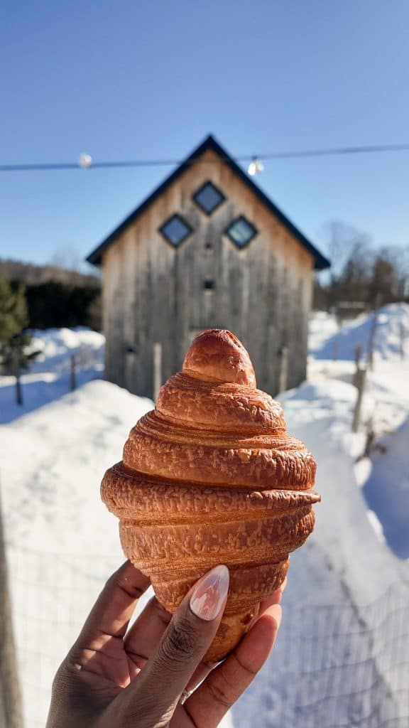 hand holding croissant in front of barn